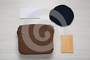 Postman hat, bag and mails on white wooden table, flat lay