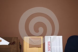 Postman hat, bag, newspapers and mails on brown background, flat lay. Space for text