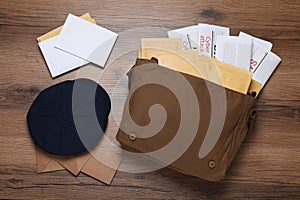 Postman hat, bag, newspapers and mails on wooden table, flat lay