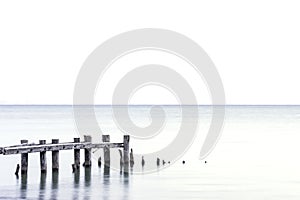 Posts of broken pier standing in a light blue lake, white sky ba