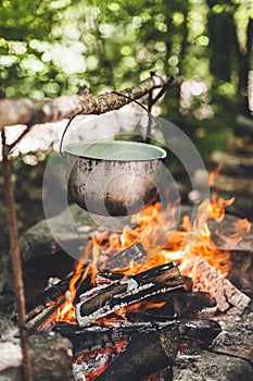 The pot is burning near the tent in the forest at night. Beautiful campfire in a tourist camp in the wild