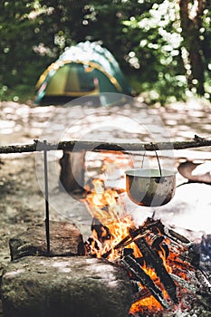 The pot is burning near the tent in the forest at night. Beautiful campfire in a tourist camp in the wild