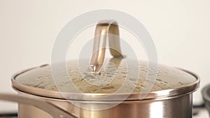 The pot is covered with a lid. Water and steam. Potatoes are boiling in a steel pan on a gas stove.