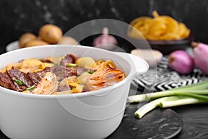 Pot of delicious vegetable soup with meat, noodles and ingredients on black wooden table, closeup. Space for text