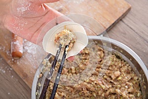 A pot of dumpling stuffing and two hands are making dumplings