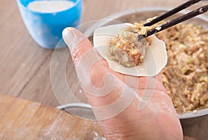 A pot of dumpling stuffing and two hands are making dumplings