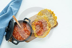 Pot with fried tomato accompanied by fried banana on a white background. Typical dish of Colombian cuisine. Copy space. PatacÃ³n