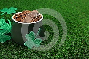 Pot of gold coins and clover leaves on grass, space for text. St. Patrick`s Day celebration