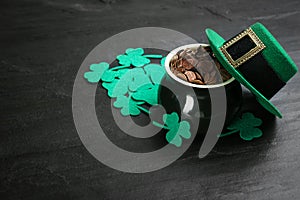 Pot of gold coins, hat and clover leaves on black stone table, space for text. St. Patrick`s Day celebration