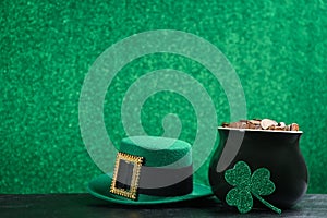 Pot of gold coins, hat and clover on stone table against green background, space for text. St. Patrick`s Day celebration