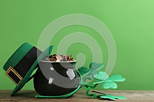 Pot of gold coins, hat and headband with clover leaves on wooden table against green background, space for text. St. Patrick`s Da