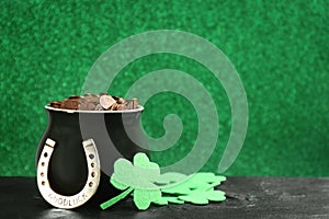 Pot of gold coins, horseshoe and clover leaves on stone table against green background, space for text. St. Patrick`s Day