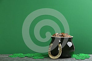 Pot of gold coins, horseshoe and clover leaves on stone table against green background, space for text. St. Patrick`s Day