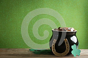 Pot of gold coins, horseshoe and clover leaves on table against green background, space for text. St. Patrick`s Day