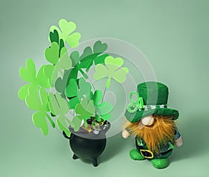 Pot of gold coins, leprechaun and clover leaves on green background, St. Patrick's Day celebration, selective focus