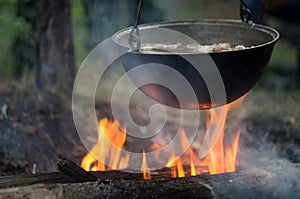 Pot with meat stew, boiling on bonfire flame, in a tourist camp in the wild forest