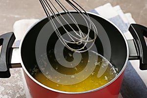 Pot with melting butter and whisk on table