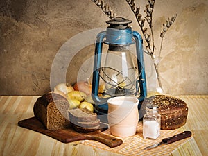 Pot of milk, rye bread, a kerosene lantern and vegetables on the table