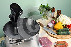 Pot with sous vide cooker, meat in vacuum packing and other ingredients on wooden table. Thermal immersion circulator