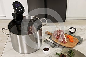 Pot with sous vide cooker and products on table indoors. Thermal immersion circulator