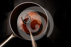 Pot and spoon with beef stock while cooking a red wine morel sauce on a black stove, dark background with copy space, high angle