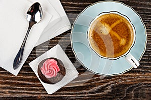 Potato cake with cream, spoon on tissue, cup of coffee on saucer on table. Top view