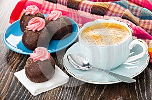 Potato cakes with cream in saucer, cake on tissue, cup of coffee, spoon on saucer, napkin on wooden table