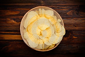 Potato chips in bowl on dark wooden table