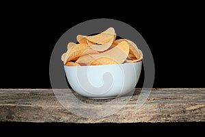 Potato chips bowl standing on old wooden plank, on black background