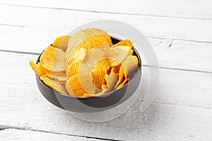 Potato chips in bowl on white wooden table.