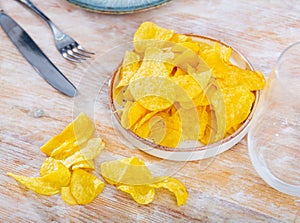 Potato chips in bowl on background. Salty crisps scattered on table