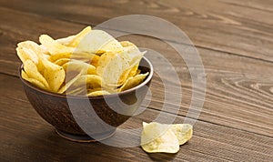 Potato chips in a bowl on wooden table.