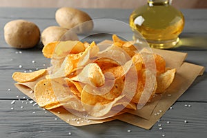 Potato chips on craft paper, sault, oliv oil, potato on gray wooden background, space for text