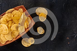 Potato chips or crisps, a salty snack in a wooden bowl, overhead flat lay shot