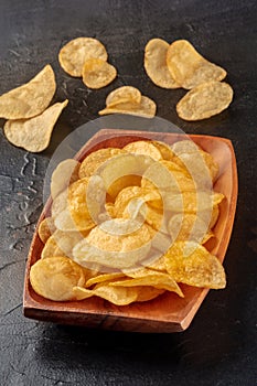 Potato chips or crisps in a wooden bowl on black