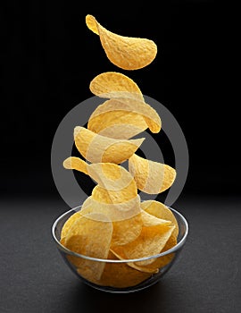 Potato chips falling into glass bowl on black background