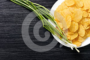 Potato chips with fresh green onion on a white plate. Rustic food background. Top view. Copy space