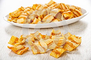 Potato chips, imitation of bacon in white dish, heap of chips on table