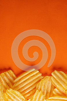 Potato chips, ribbed and fluted, shot from above on a bright orange background. vertical layout and concept, copyspace