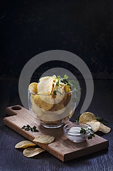 Potato chips with sauce on a cutting board, on a dark background, with a copy of the space