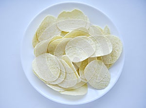 Potato chips in a saucer on a white background. They pour the chips out of the box. A delicious snack