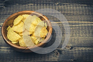 Potato chips in a wooden bowl on a dark background/potato chips in a wooden bowl on a dark background. Top view. Copy space