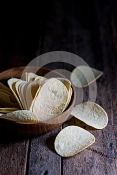 Potato chips in a wooden bowl on a rustic wooden floor.