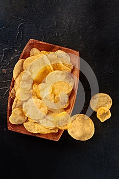 Potato chips in a wooden bowl, salty crisps, shot from the top on black