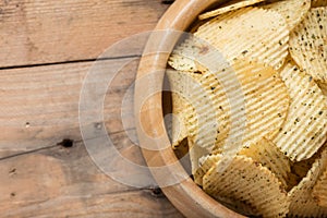 Potato chips in a wooden bowl on wood background.