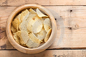 Potato chips in a wooden bowl on wood background.