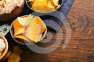 Potato corrugatedchips. Fast food. Crispy potato chips ceramic black bowl with sour cream sauce and onions in wooden stand on old