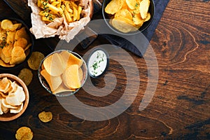 Potato corrugatedchips. Fast food. Crispy potato chips ceramic black bowl with sour cream sauce and onions in wooden stand on old