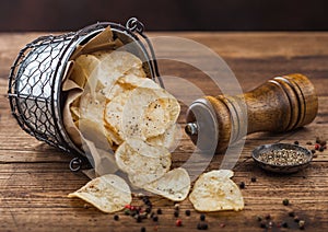 Potato crisps chips snack with black pepper snack bucket on dark background with mill and ground pepper