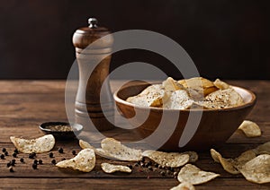 Potato crisps chips snack with  black pepper in wooden bowl on dark background with mill and ground pepper